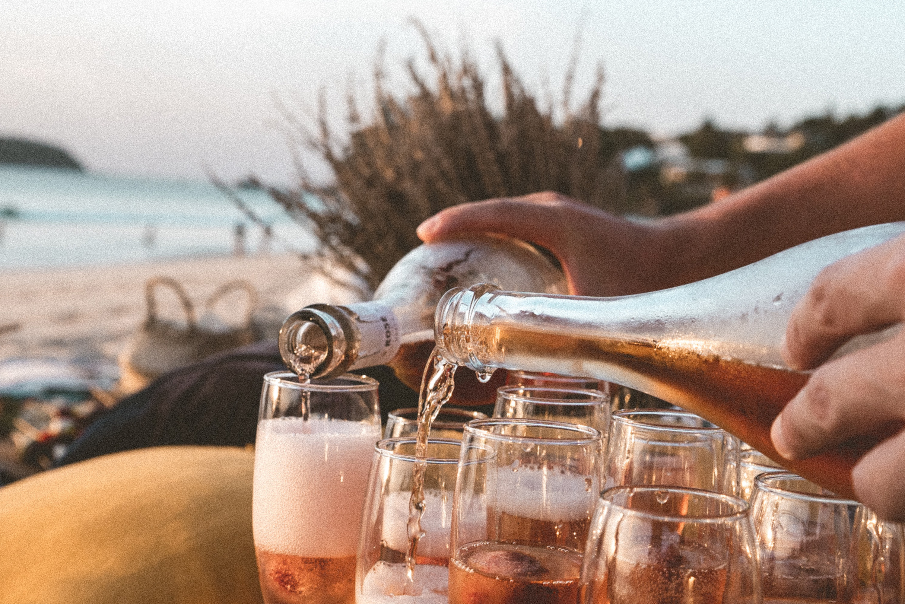 Couple pouring pink champagne in flutes at the beach.