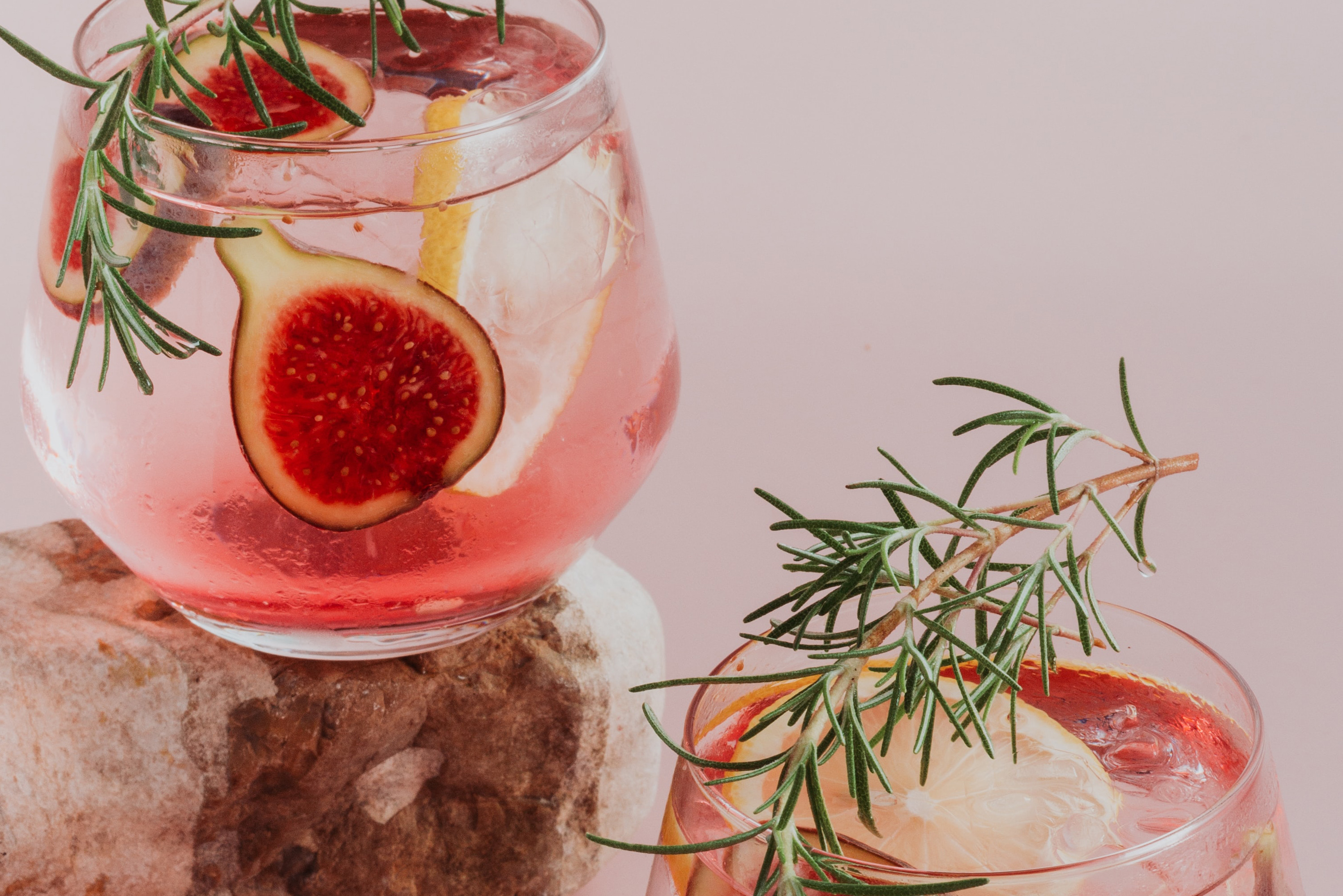 Two cocktails with figs and rosemary sprigs inside the glass.